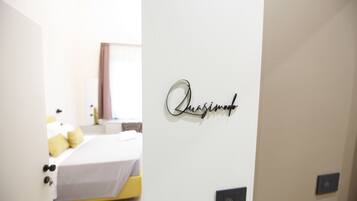 A hotel room with a bed, a bedside table, and a wall-mounted sign.