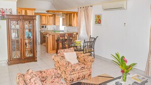 A living room with floral-patterned sofas, a dining table with chairs, a kitchen area with wooden cabinets, and an air conditioning unit on the wall. - Bamboo Villa  (St. Ann's Bay)