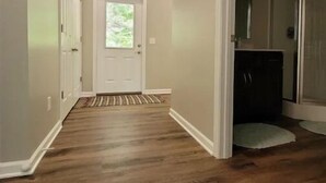 Un couloir au sol en bois, une porte blanche au fond et un luminaire au plafond.