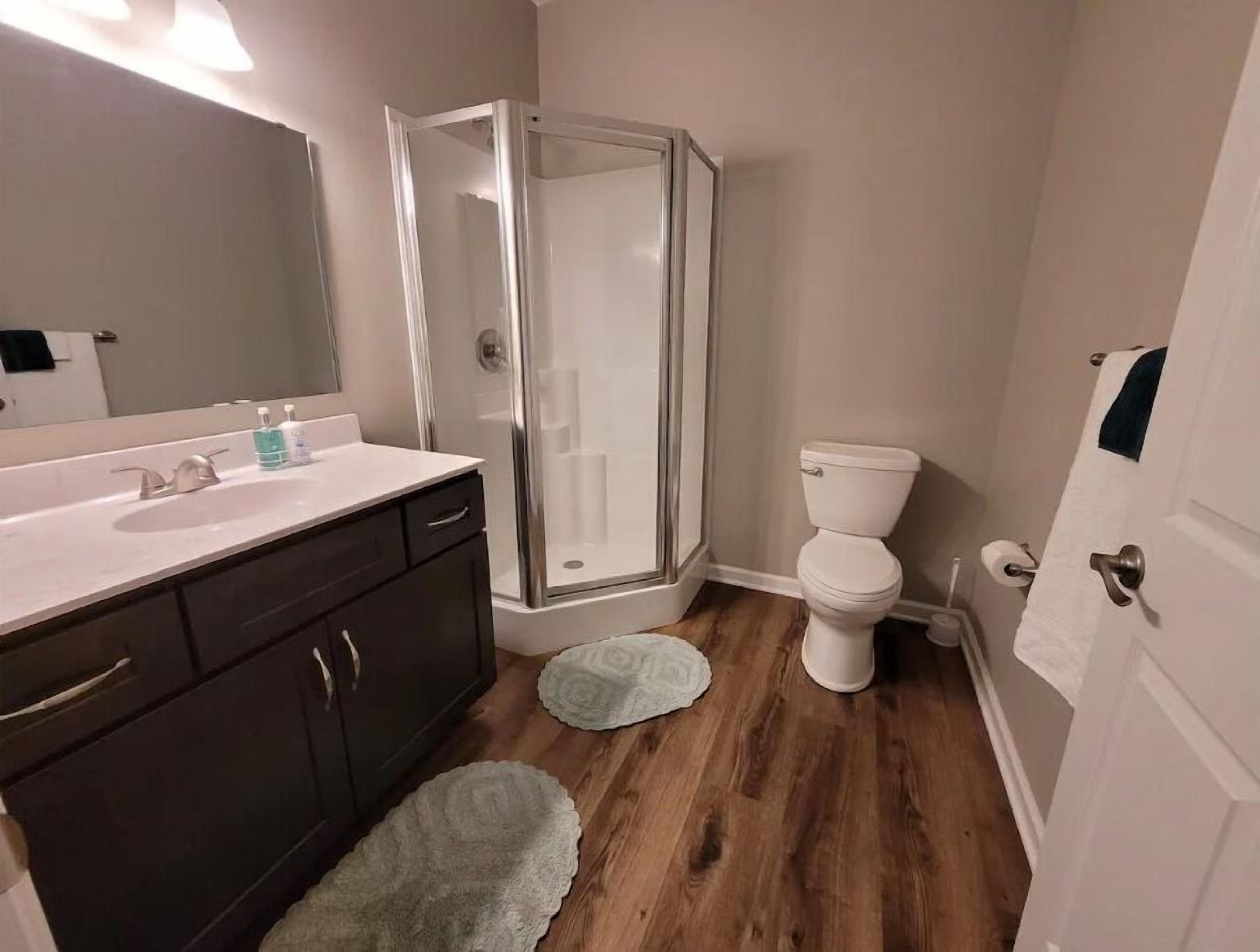 A bathroom with a shower, toilet, sink, and dark cabinets.