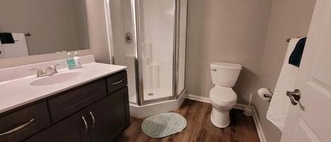 A bathroom with a shower, toilet, sink, and dark cabinets.