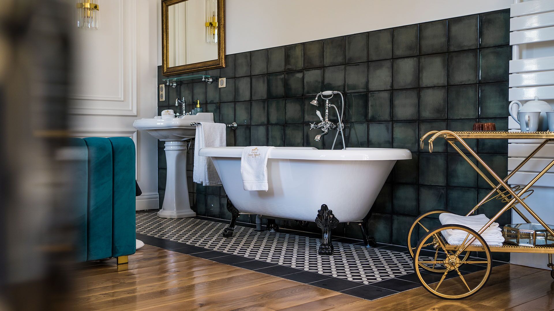 Ein Badezimmer mit freistehender Badewanne, Waschtisch und spiegel mit goldener Rahmung.