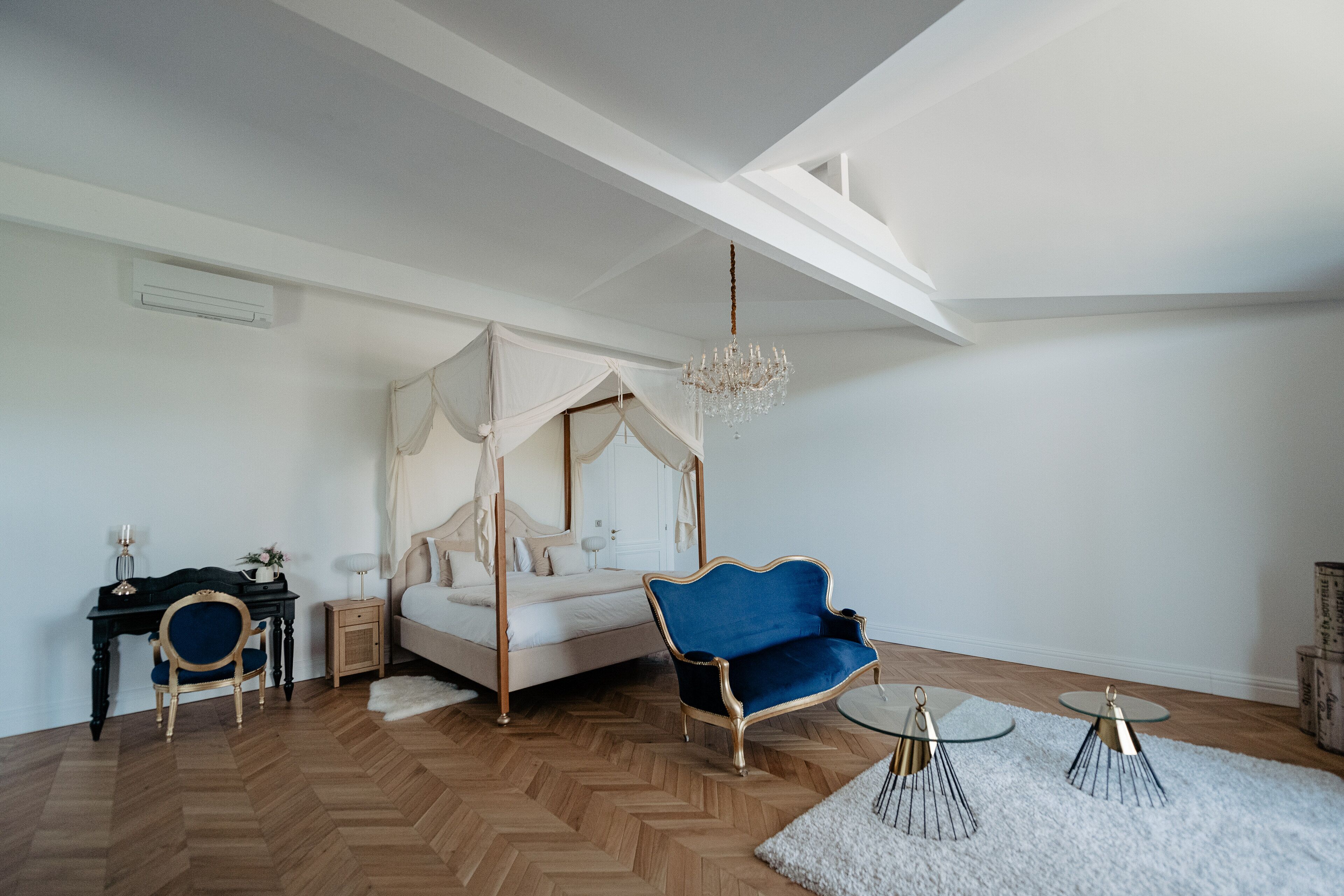 Une chambre à coucher avec un lit à baldaquin, un fauteuil bleu, un bureau avec une chaise et un lustre.