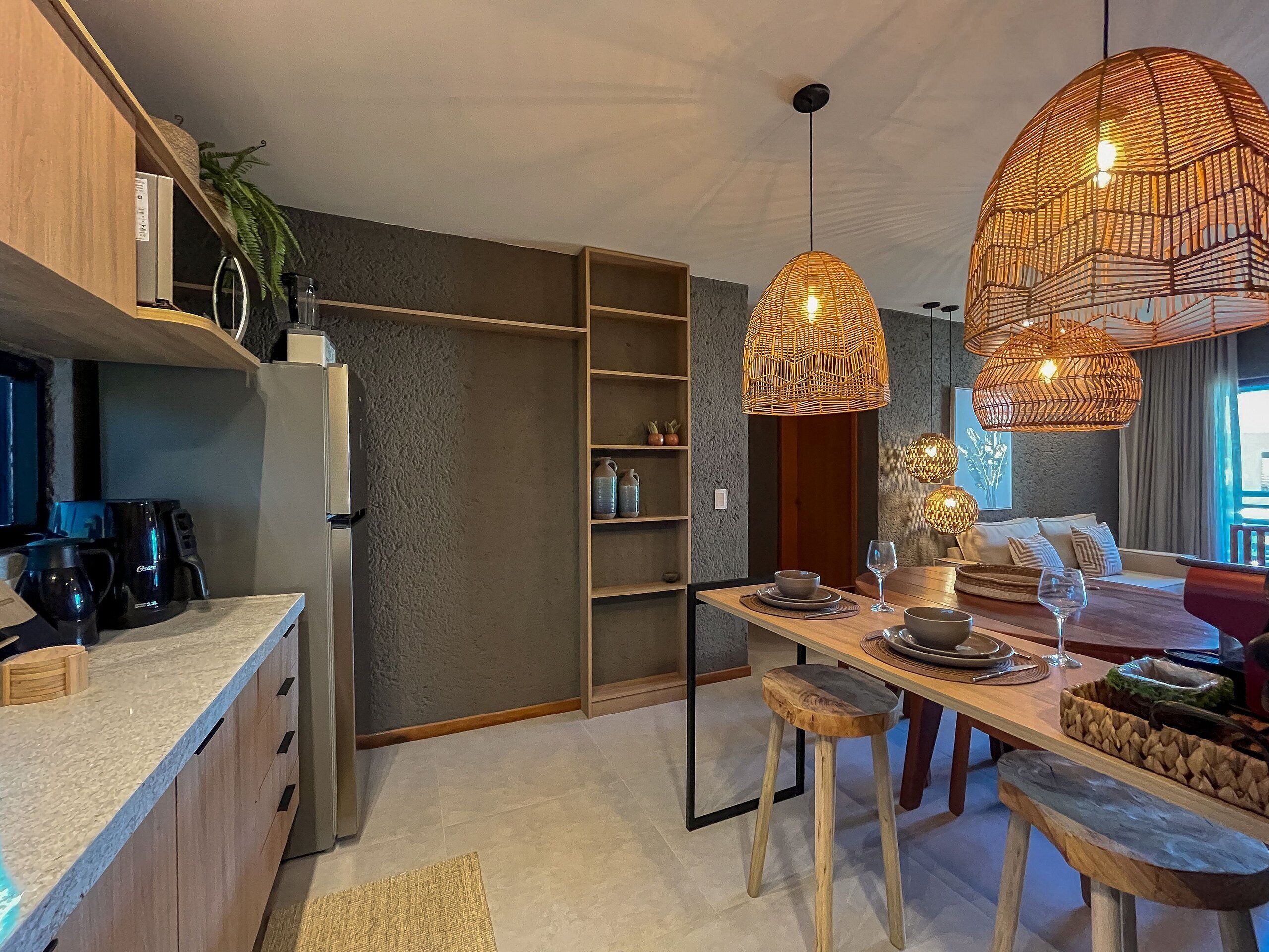 Eine moderne Küche mit integriertem Kühlschrank, einer Kaffeemaschine und einem Essbereich mit einem Holztisch und Hockern.