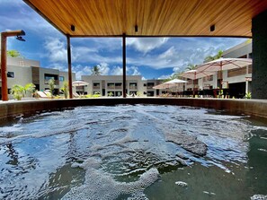 Une piscine surmontée d’une structure en bois, entourée de bâtiments modernes et agrémentée d’espaces de détente en plein air.