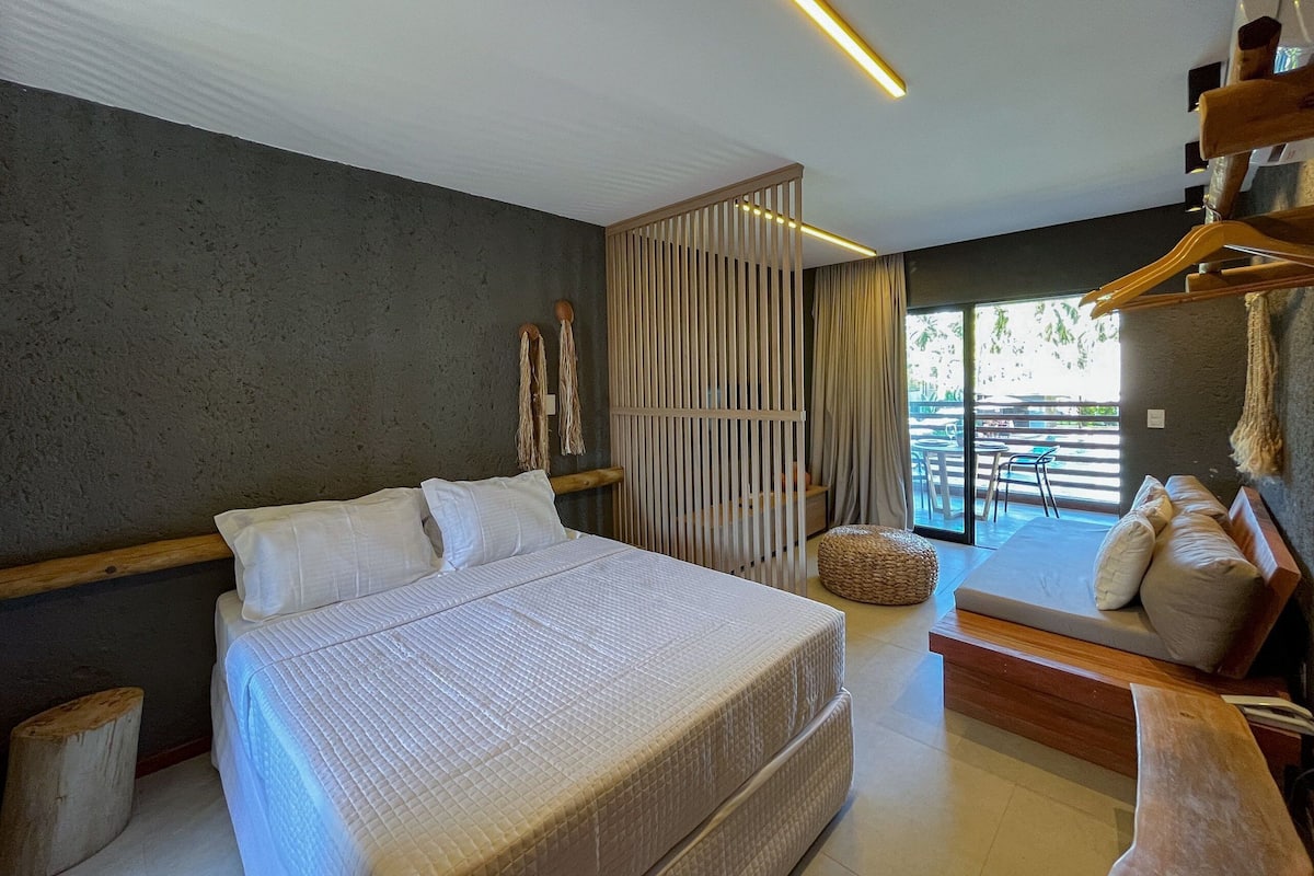 A modern bedroom with a large bed, a wooden bench, and a view of the outdoors.
