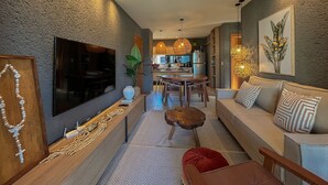 A modern living room with a sofa, a coffee table, a TV, and a dining area with a table and chairs. - Villas Manatee by ER (Porto de Pedras)