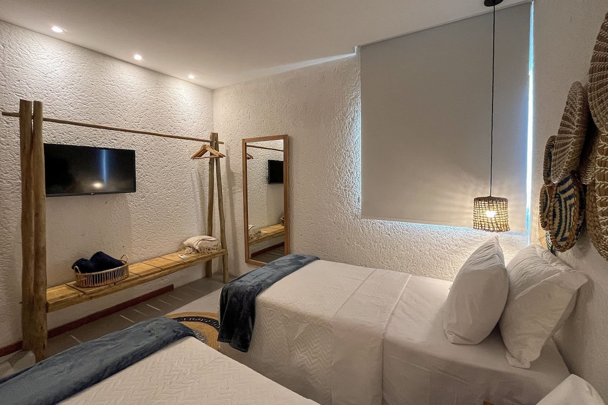 A bedroom with two beds, a TV, a mirror, and a window with a view.