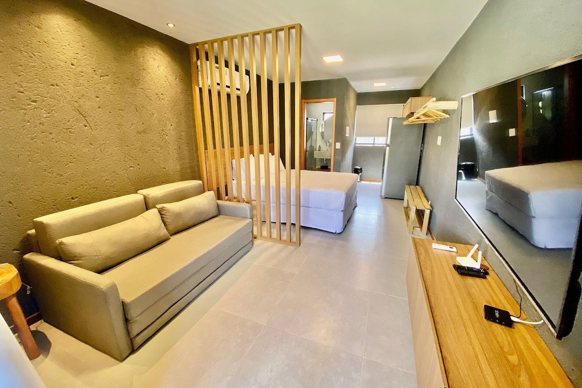 A modern hotel room with a sofa, a bed, a TV, and a wooden partition.