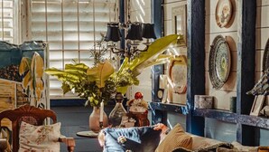Ein gemütliches Zimmer mit einem Vintage-Sofa, einem Holztisch und einem großen Fenster mit Jalousien.