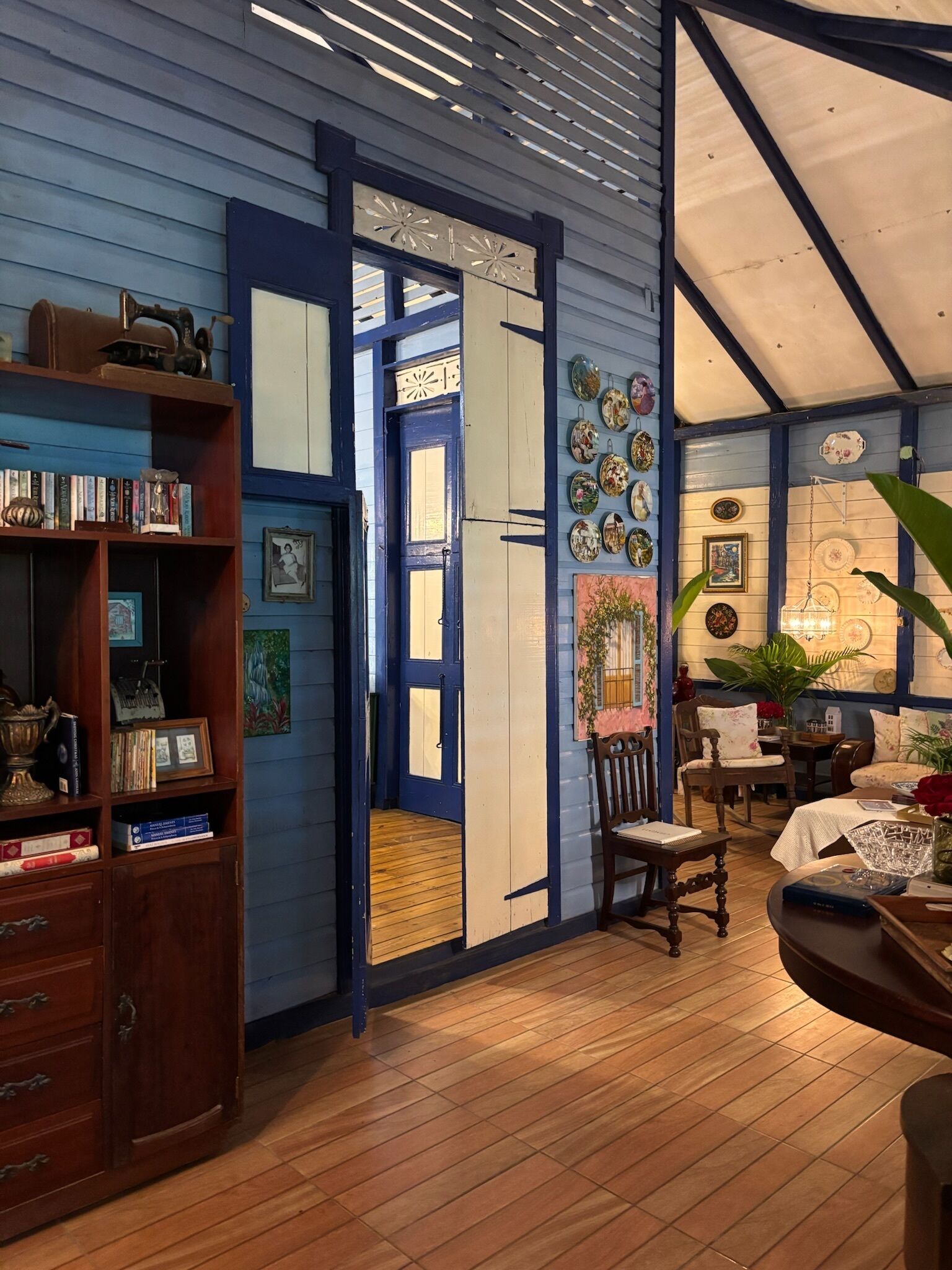 Una habitación con suelo de madera, una estantería, una puerta con paneles decorativos y una pared con diversos objetos.