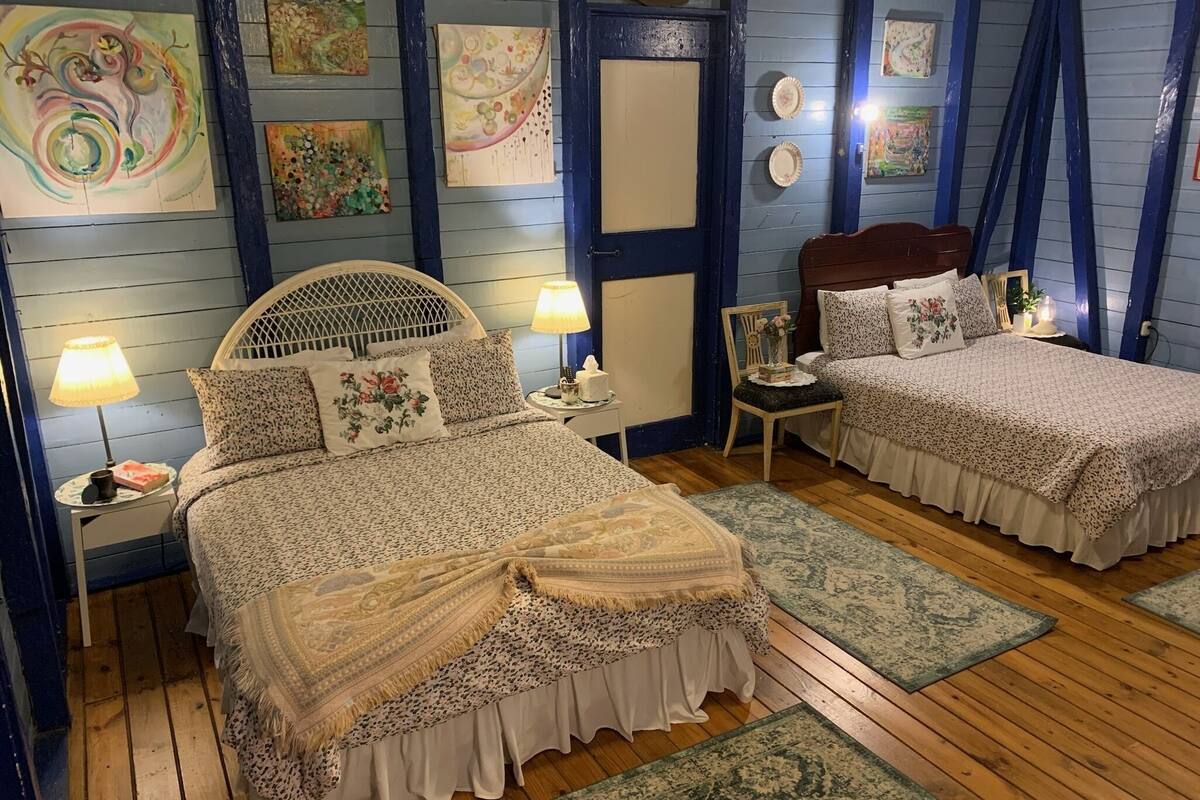 A bedroom with two beds, wooden flooring, and artwork on the walls.