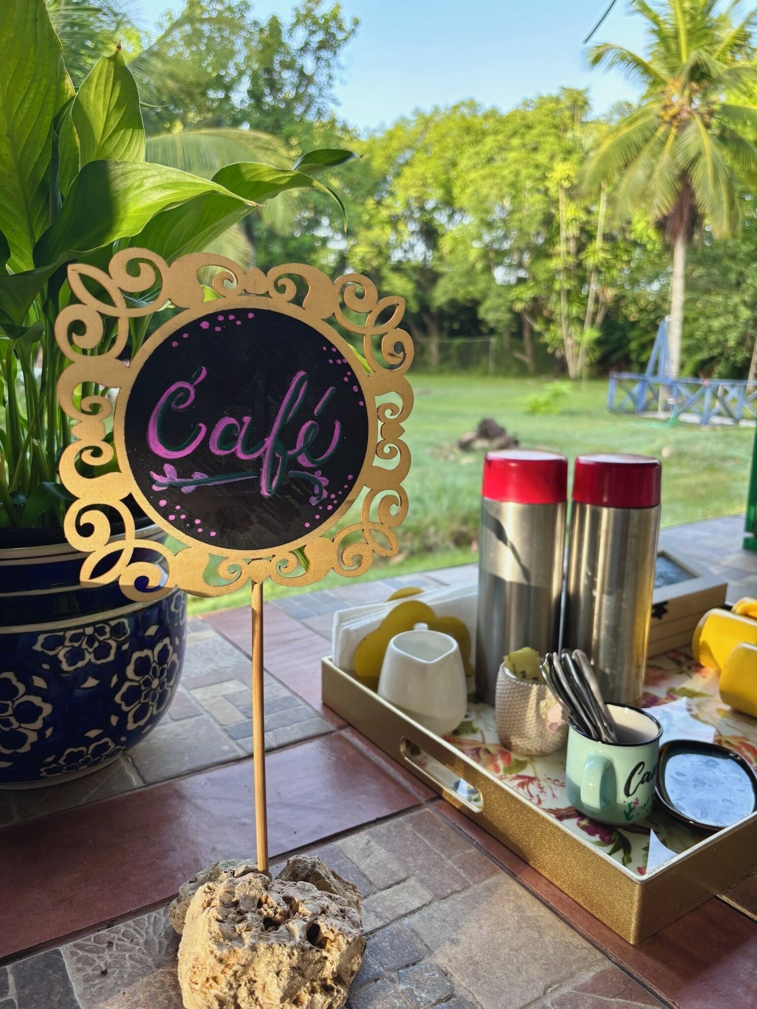 Placa de café com moldura decorativa, uma planta em vaso e uma bandeja com utensílios e acompanhamentos.
