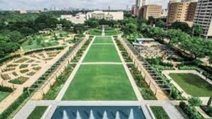 Une vaste cour ouverte, avec une fontaine centrale, entourée de verdure et de sentiers.