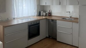 A modern kitchen with grey cabinets, a wooden countertop, a built-in oven, a dishwasher, and a window with sheer curtains. - 3 Zimmer EG Ferienwohnung mit Balkon - mit 65 qm (Nürnberg)