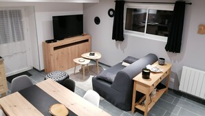 A modern living room with a sofa, a TV, a small table, and a dining table.