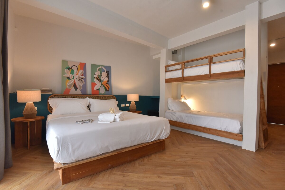 Quarto de hotel com uma cama grande, uma cama menor em um mezanino, duas mesas de cabeceira com luminárias e obras de arte na parede.