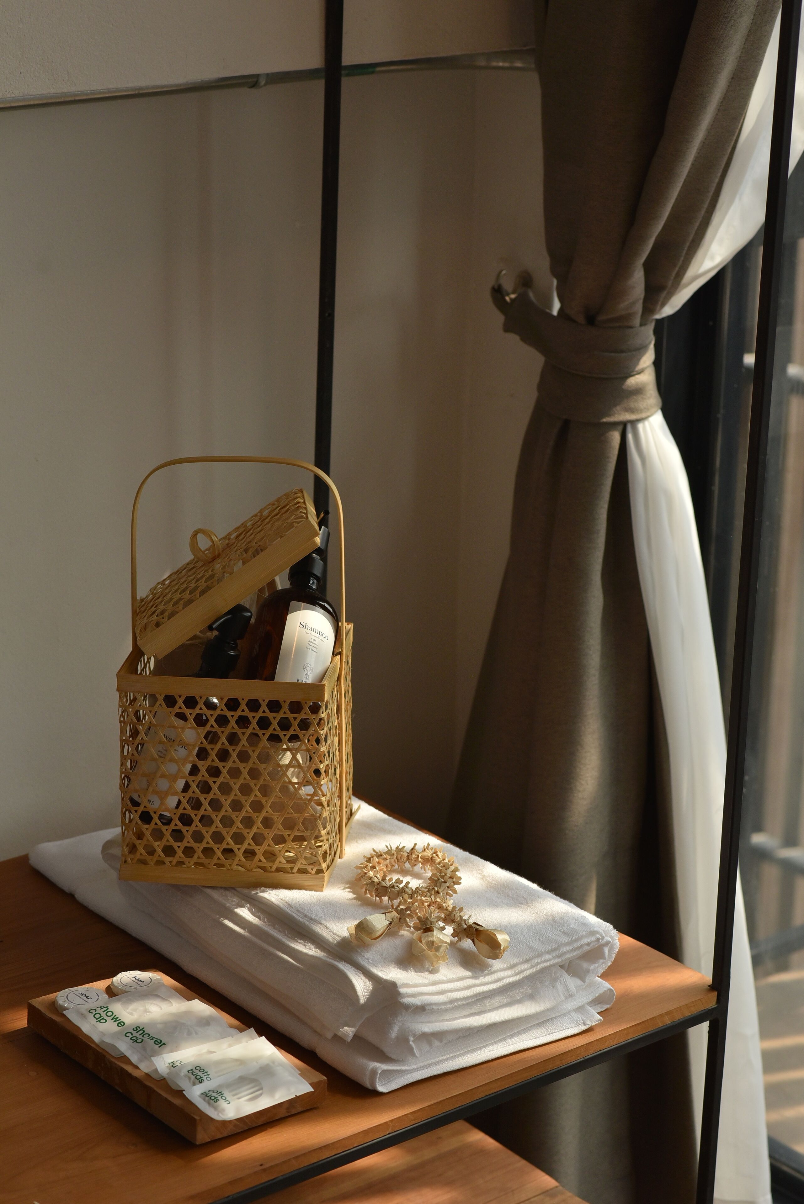 A wicker basket with toiletries on a wooden table next to a window with curtains.