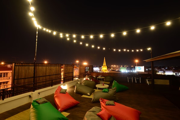 A rooftop terrace with string lights, outdoor seating, and a view of a cityscape at night. - KWANS Ayutthaya (Ayutthaya)