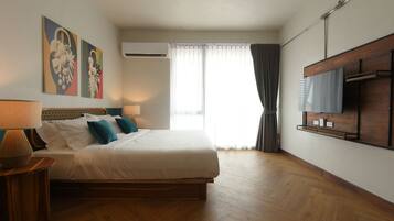 A hotel room with a large bed, a TV mounted on the wall, and a window with curtains.