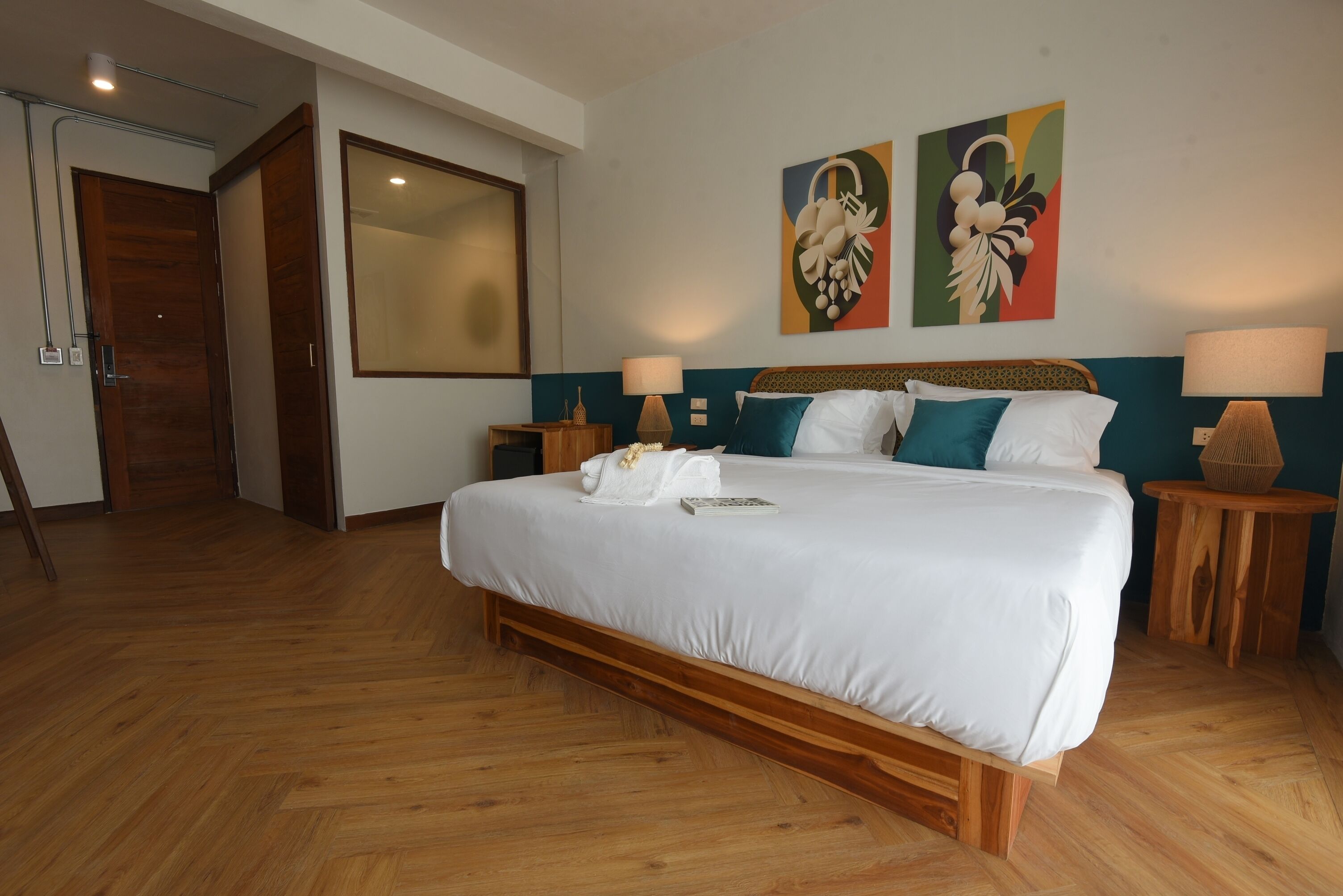 Una habitación de hotel con una cama grande, suelo de madera, dos mesitas de noche, un espejo y dos cuadros colgados en la pared.