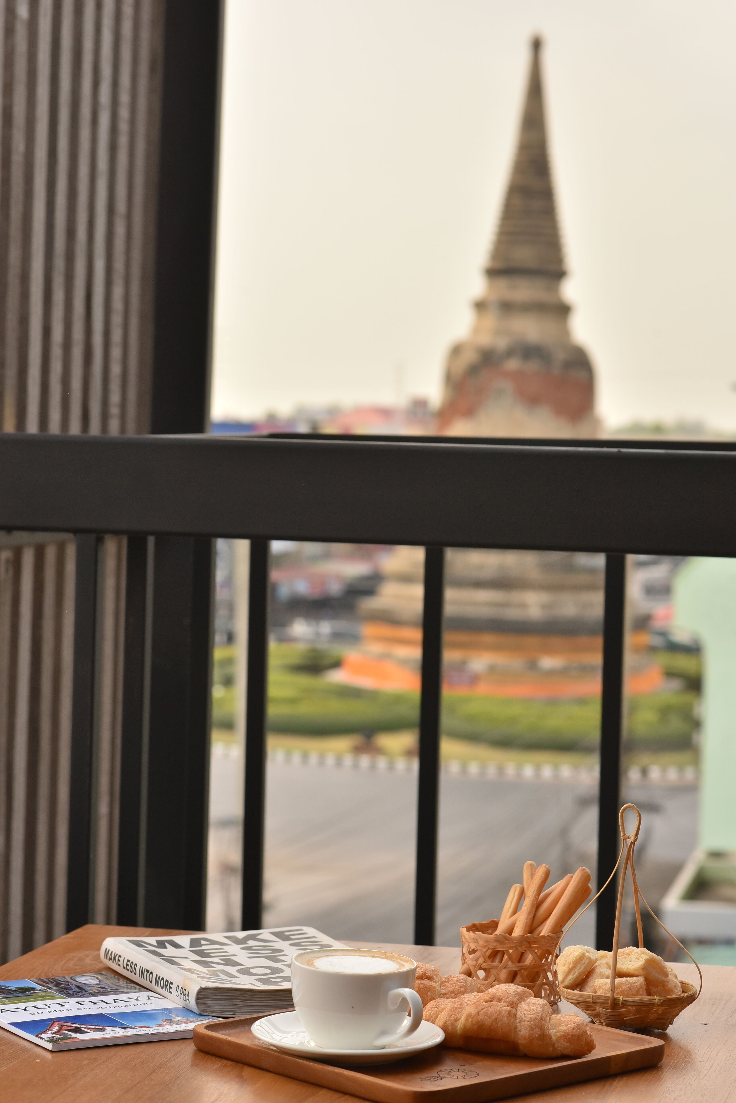 Een tafel met een kop koffie, croissants en een mandje stokbrood op een balkon met uitzicht op een stadsbeeld en een opvallende toren.