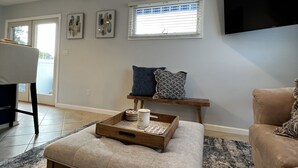 Ein Wohnzimmer mit Couch, Fernseher an der Wand und einem Tisch aus Holz, ein Fenster mit Jalousien.