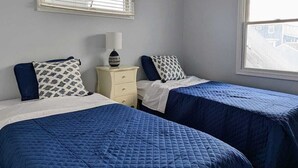 Ein Zimmer mit zwei Betten, einem Nachttisch, einem Fenster mit Jalousien und einer Deckenleuchte.