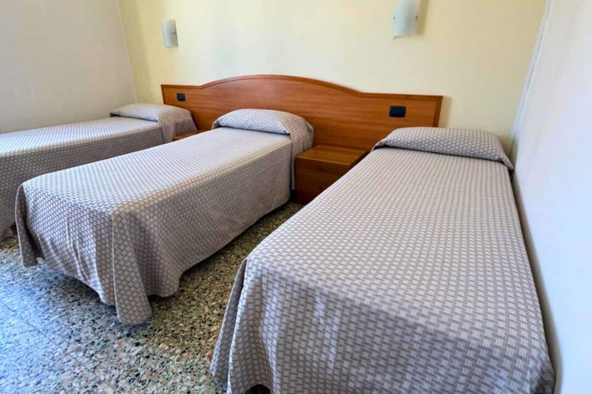 A room with three single beds, a wooden headboard, a wall-mounted light, and a framed picture.