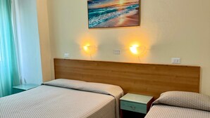 A hotel room with two beds, a wooden headboard, a painting of a beach scene, and two wall-mounted lights. - Hotel Valente (Ortona)