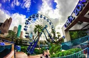 Experience the thrill of a large Ferris wheel in a scenic outdoor setting surrounded by lush greenery and a nearby building.