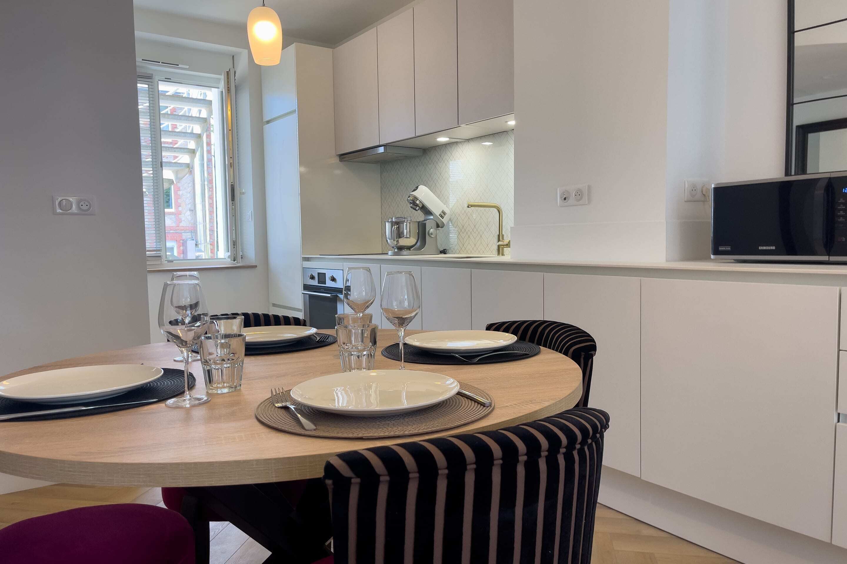 A modern kitchen with white cabinets, a microwave, and a dining area with striped chairs and a round table set for two.