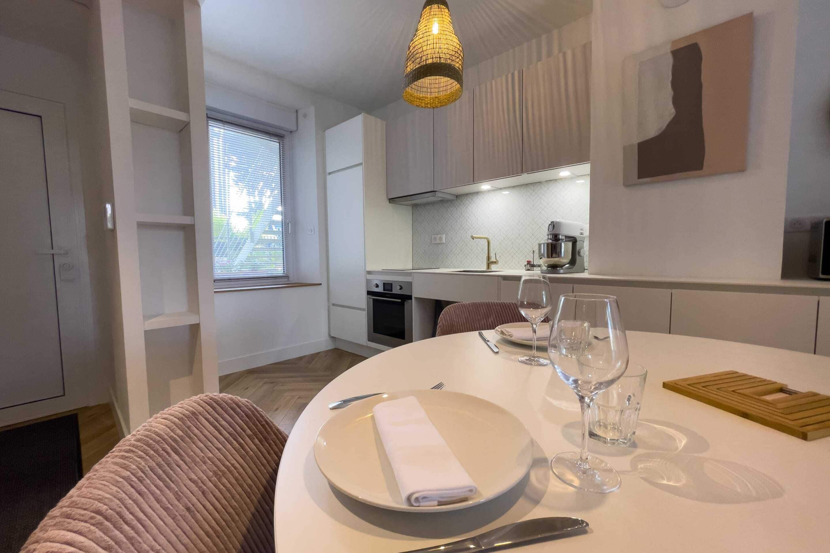 A modern kitchen with white cabinets, a built-in oven, and a dining area with a round table set for two.