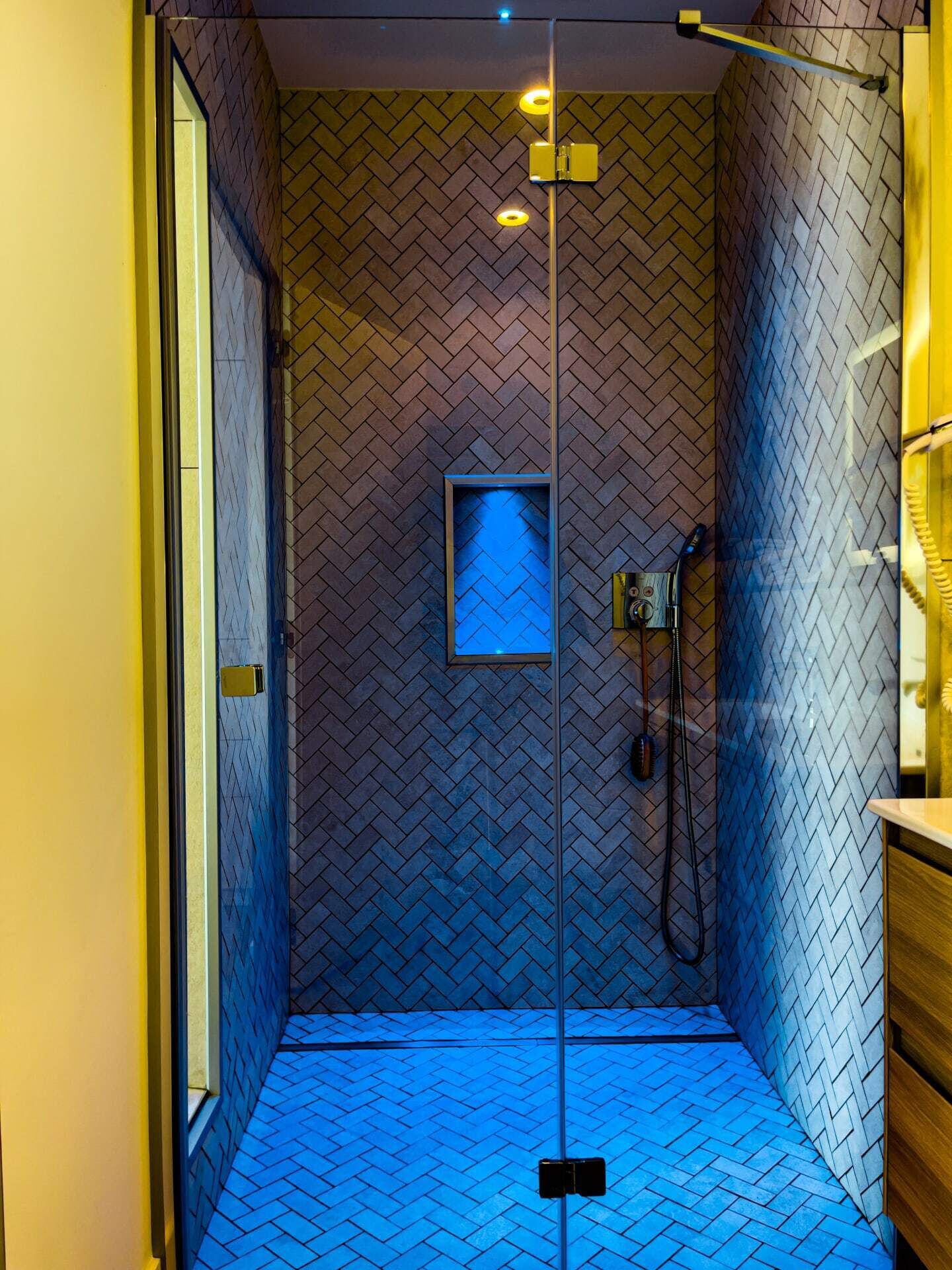 A modern shower with a herringbone tile pattern, a glass door, and a built-in showerhead.