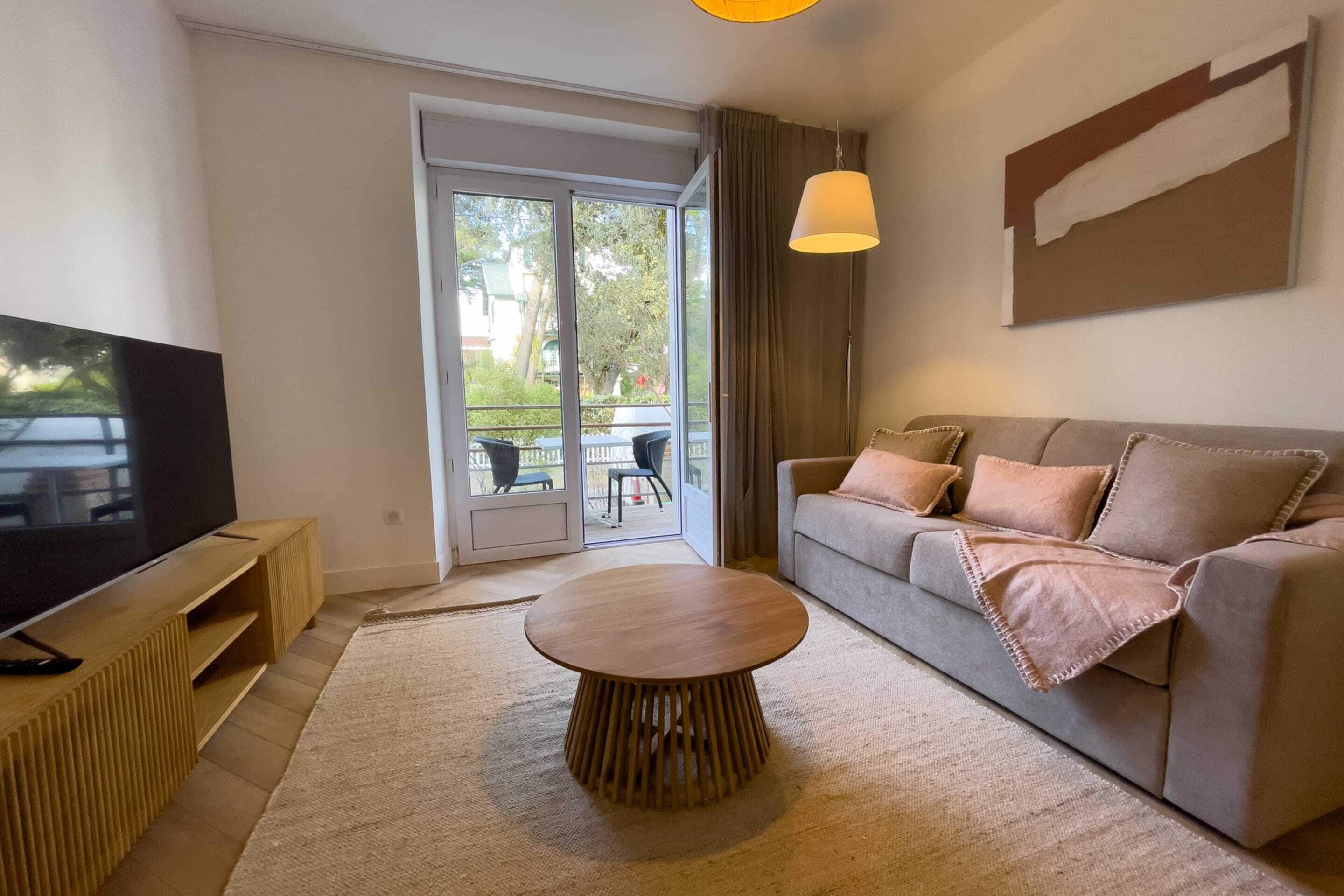 A modern living room with a sofa, a coffee table, a TV, and a sliding glass door leading to an outdoor area.
