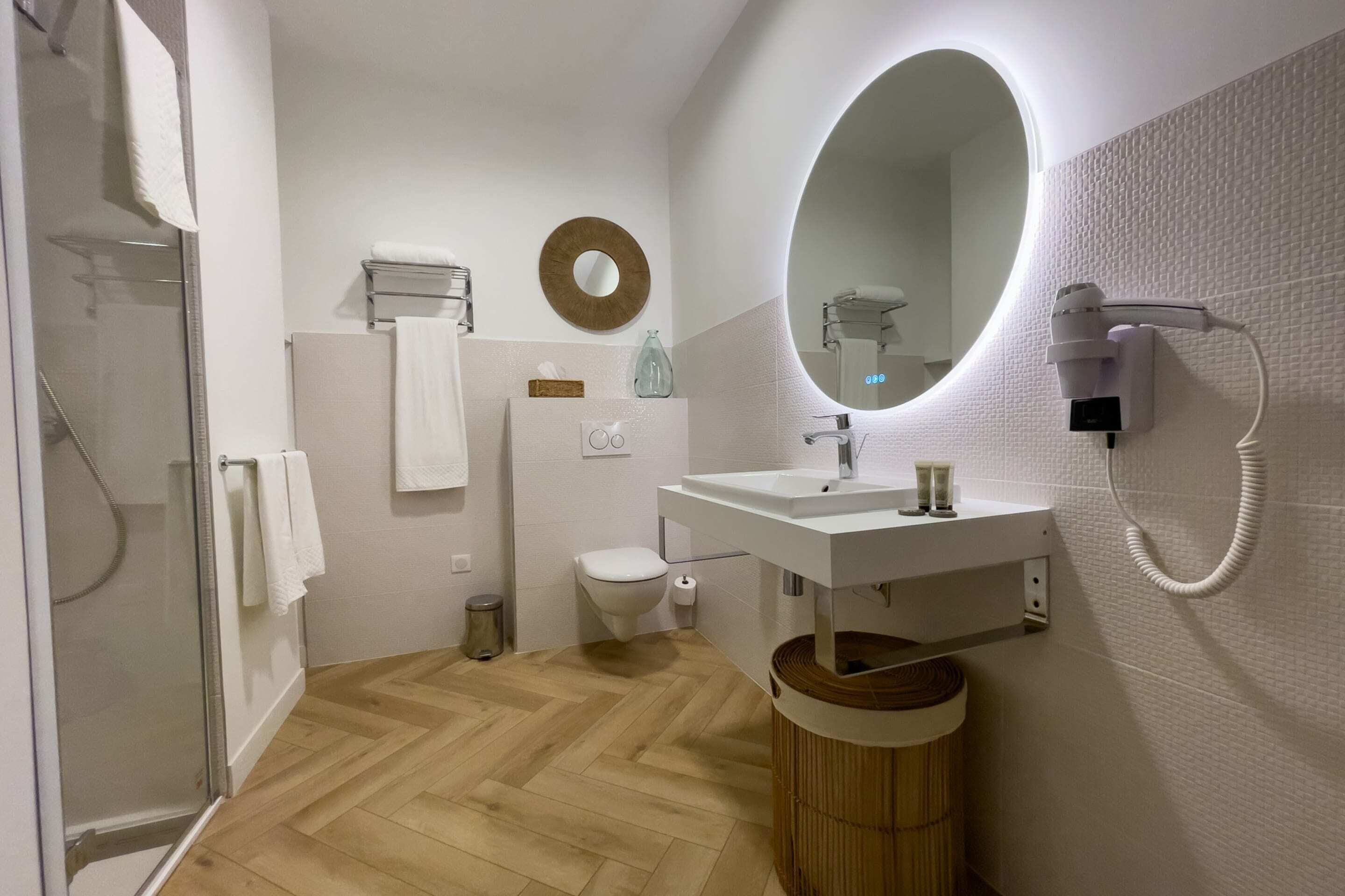 A modern bathroom with a glass shower enclosure, a white sink with a mirror above, and a wooden floor.