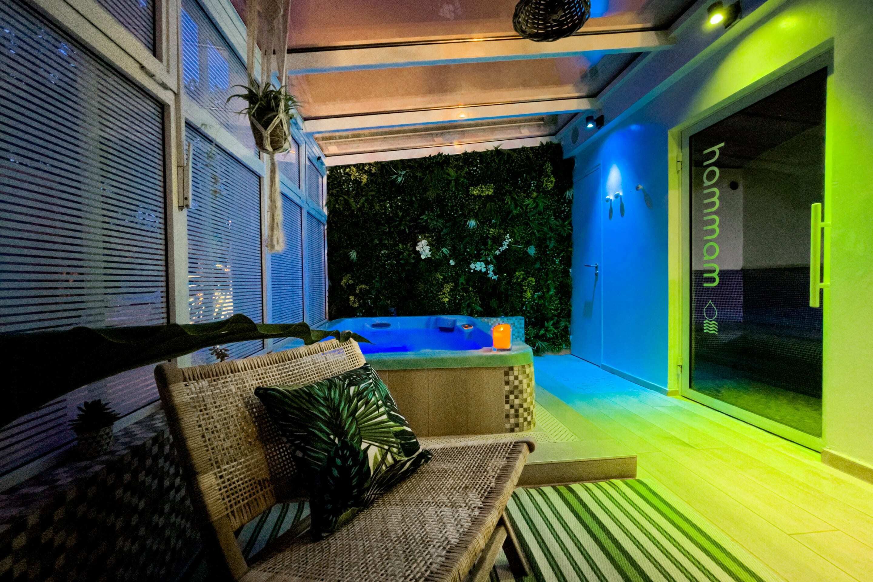 Un espace extérieur accueillant avec un canapé en osier et une petite table, un jacuzzi et un mur végétalisé.