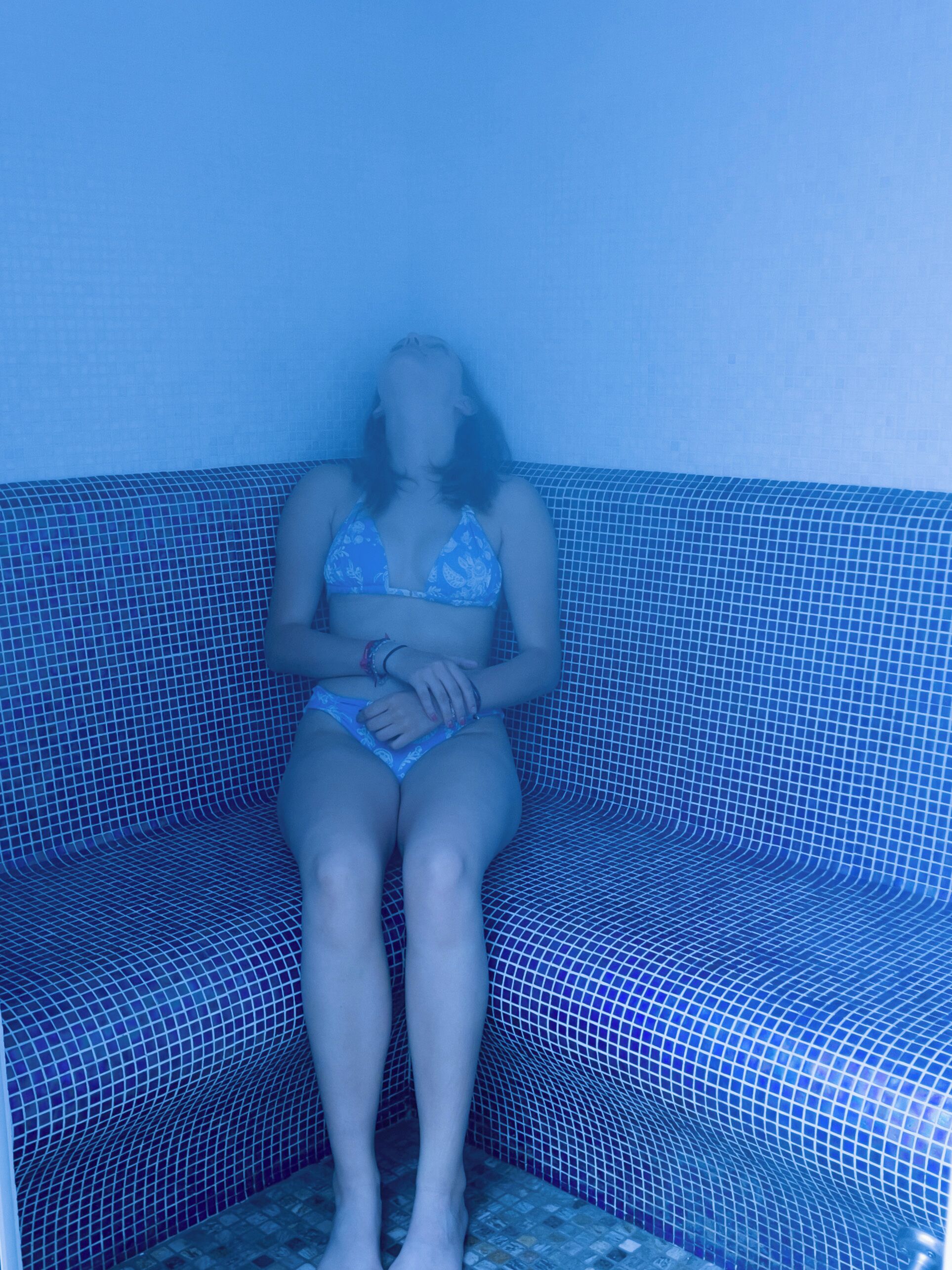 A person sitting on a blue tiled bench with a patterned design.