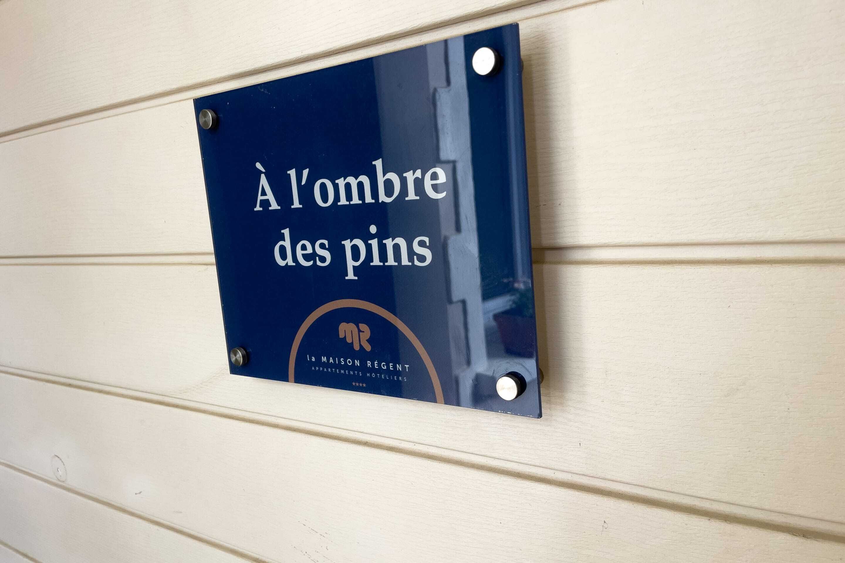 A sign with the text "À l'ombre des pins" and the logo of "la maison régent" on a wall.