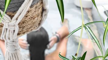 A macrame hanging planter with green plants, a person sitting on a stone bench, and a stone wall in the background.