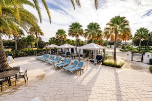 A poolside area with lounge chairs, umbrellas, and palm trees.