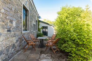 A stone building with a patio area featuring a table and four wooden chairs. - The Old Stables at Moyglare Manor (Maynooth)