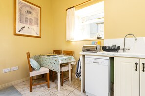 A kitchen with a dining table, chairs, a window with curtains, a sink, and a dishwasher. - The Old Stables at Moyglare Manor (Maynooth)