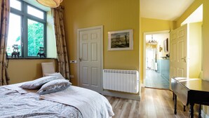 Une chambre à coucher avec un lit, un radiateur, une porte et une fenêtre avec des rideaux.
