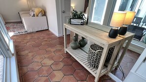 A room with a hexagonal tile floor, a wooden console table with a welcome sign, a sofa, and a lamp.