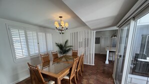 A dining area with a glass-top table surrounded by wooden chairs, a chandelier, and a potted plant.