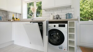 Ett kompakt kök med en inbyggd tvättmaskin och torktumlare, ett fönster med utsikt över grönområden och en bänkskiva med en flaska och en banan.