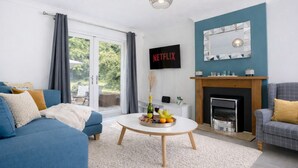Ett modernt vardagsrum med en soffa, fåtölj, soffbord, öppen spis och en tv-skärm som visar "NETFLIX".