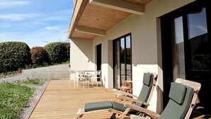 A modern outdoor patio with wooden flooring, lounge chairs, and a table. - Appartement Contemporain Avec Terrasse à 5mn de du lac D'annecy (Doussard)