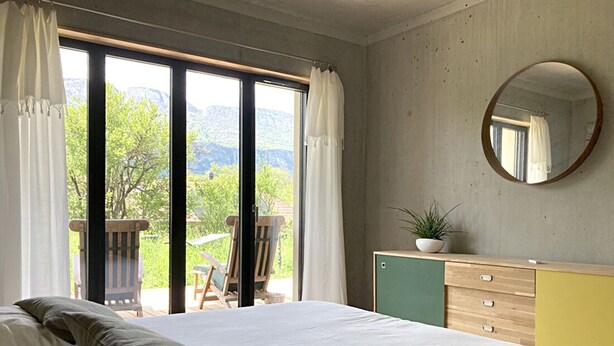A bedroom with a large bed, a dresser, a mirror, and a view of greenery and mountains through the window. - Appartement Contemporain Avec Terrasse à 5mn de du lac D'annecy (Doussard)